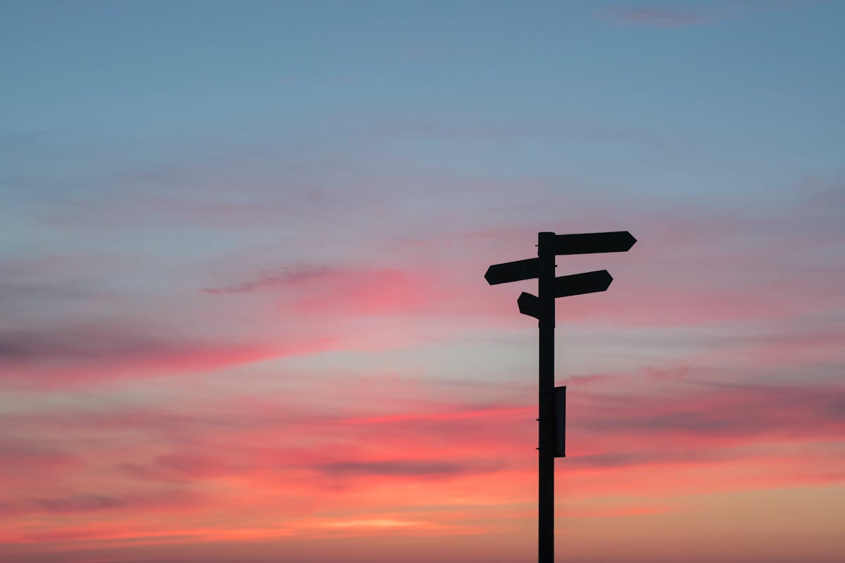 Silhouette of a sign pointing in multiple directions in front of a sunset